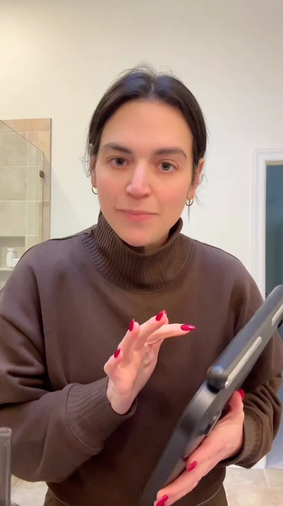 Person wearing a brown turtleneck sweater holding a hair straightener indoors.